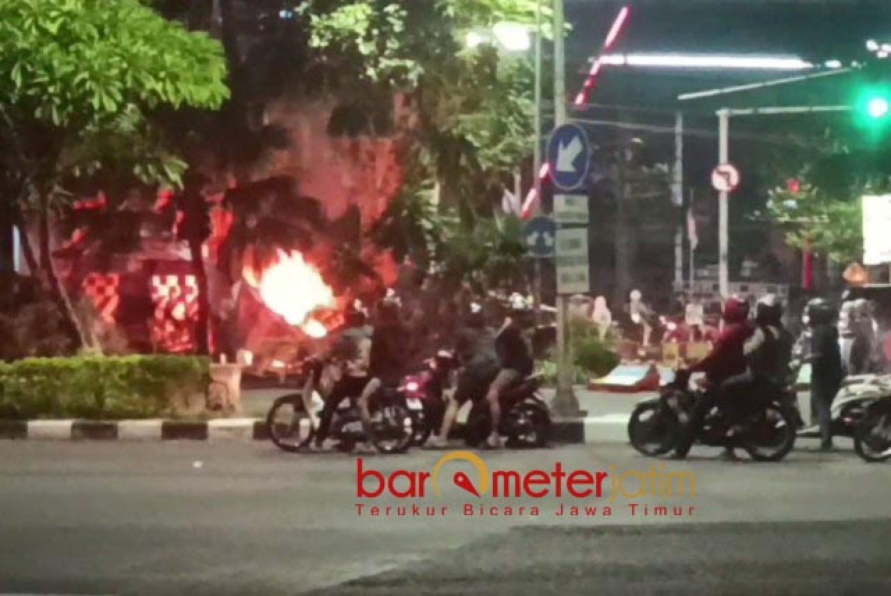 TOTONAN: Pengguna jalan saksikan pos polisi di Taman Pelangi yang dibakar massa pendemo. | Foto: Barometerjatim.com/BKT